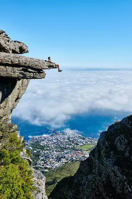 A person sitting on top of a cliff above the ocean.