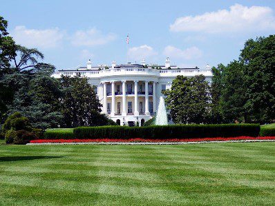 A white house with trees and bushes in front of it.