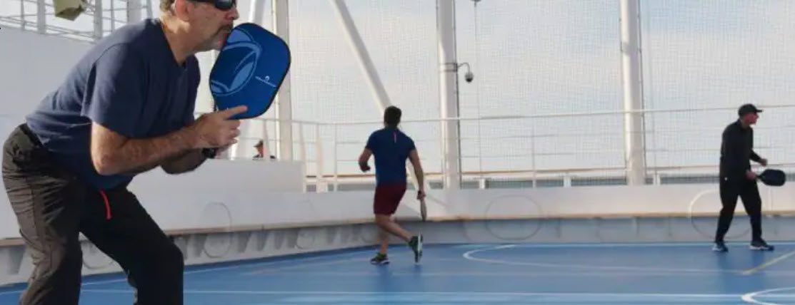 A man is playing tennis on the deck of a boat.