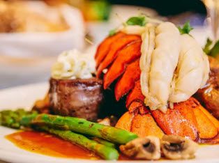 A plate of food with meat, vegetables and lobster.