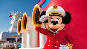 A mickey mouse character saluting in front of the disney cruise ship.