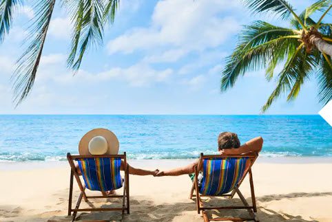 Two people sitting on a beach holding hands.