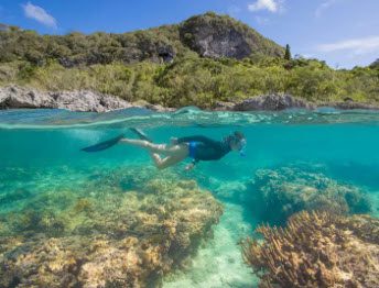 A person swimming in the ocean near some rocks.