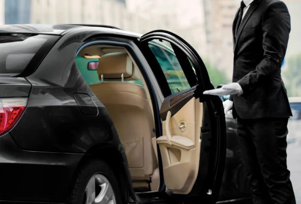 A man in black suit and white gloves standing next to a car.